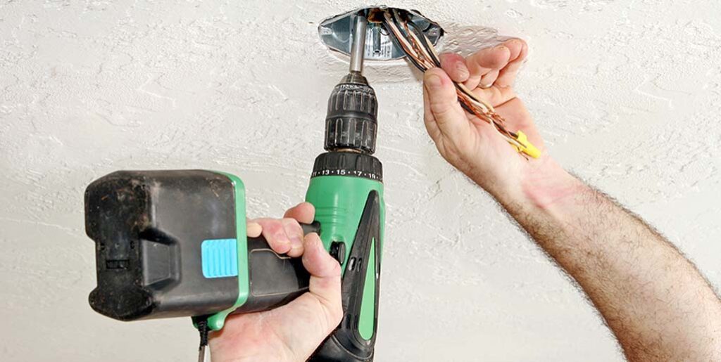 Man using drill to secure wiring for smoke alarm.